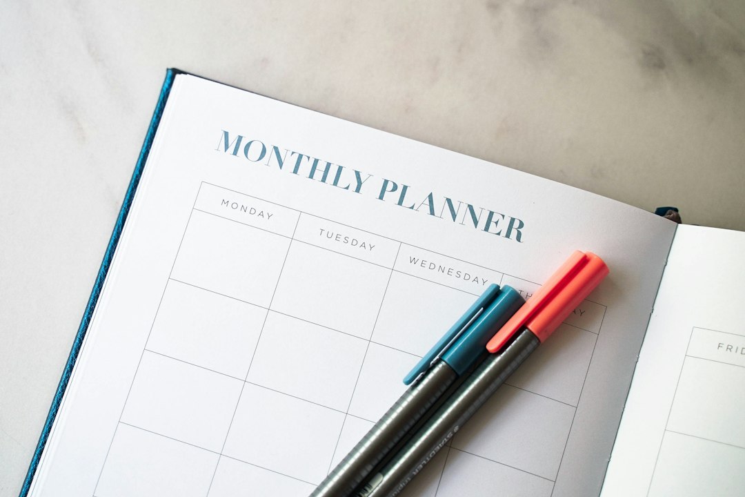 Agenda mensuel ouvert sur une page blanche, avec deux stylos posés dessus