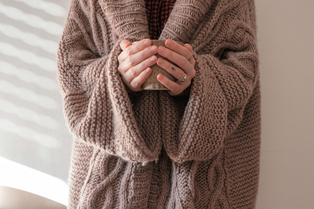 Deux mains tenant une tasse chaude, enveloppées dans un gros pull en laine beige